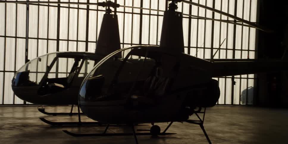 Two men talk in a hangar as a helicopter is moved across the floor