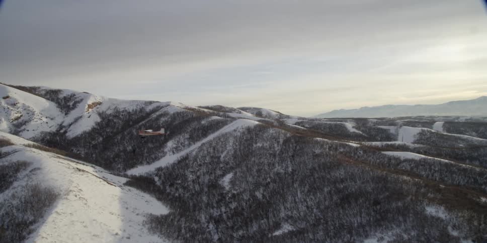 An airplane flying over snow covered hills
