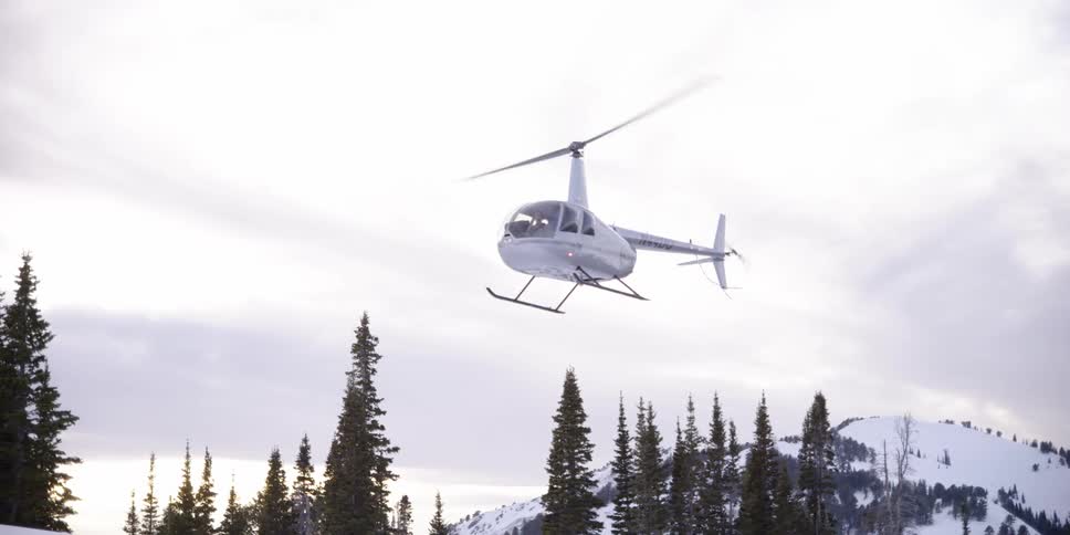 Helicopter pilot lands a white helicopter on a snowy field