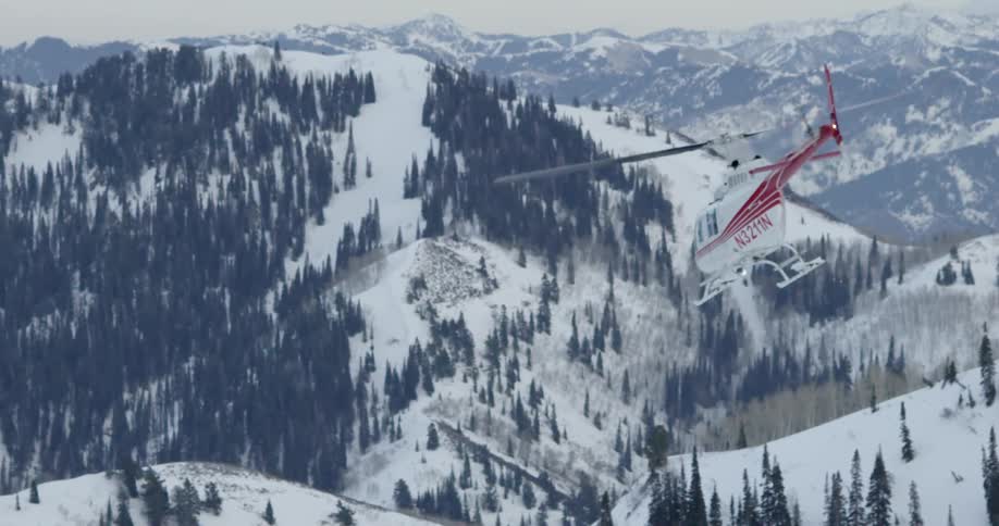 Helicopter with large blades flies over the snow capped high mountains