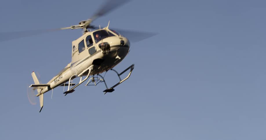 A helicopter flies over a red rock formation in a bright blue sky