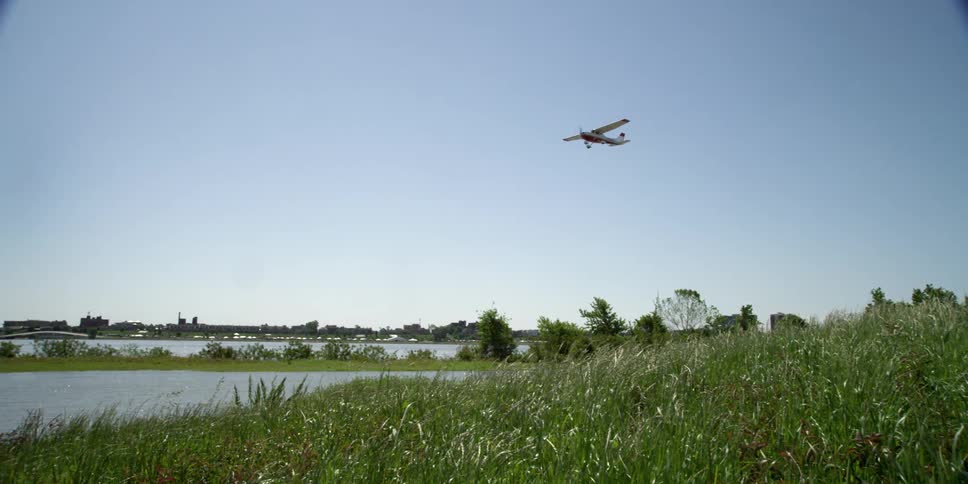 A small airplane flies over a river near a city