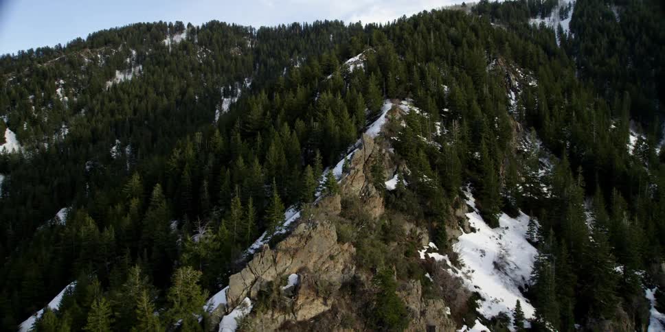 A helicopter flies over a mountain range with patches of snow
