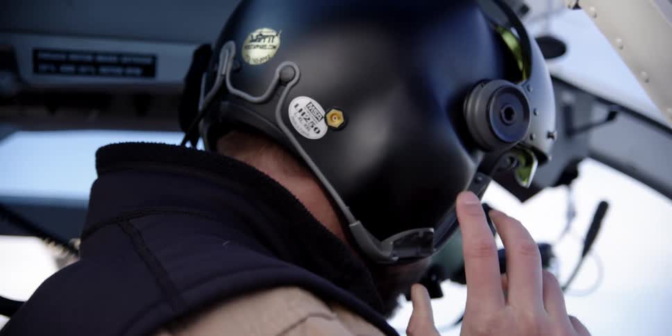 A man in a helicopter adjusting his helmet