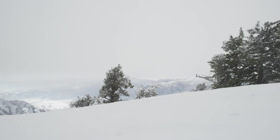 Helicopter flies over the snow capped mountains as it snows