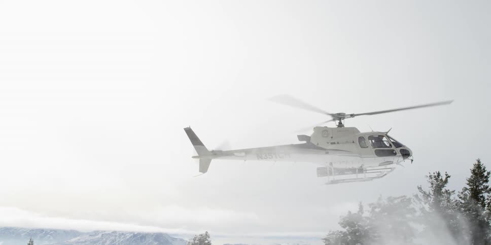 Helicopter with large blades comes down through the air onto the snowy ground