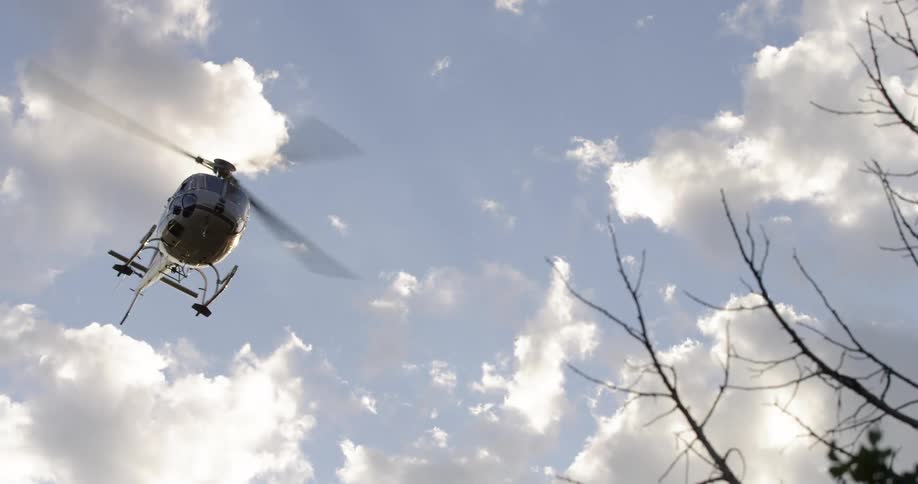 A helicopter flying in the sky with trees in the foreground and the sky in the background