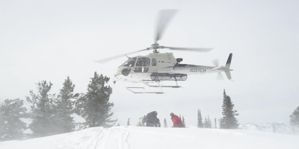 Three people sit on the ground as a helicopter lifts off above them
