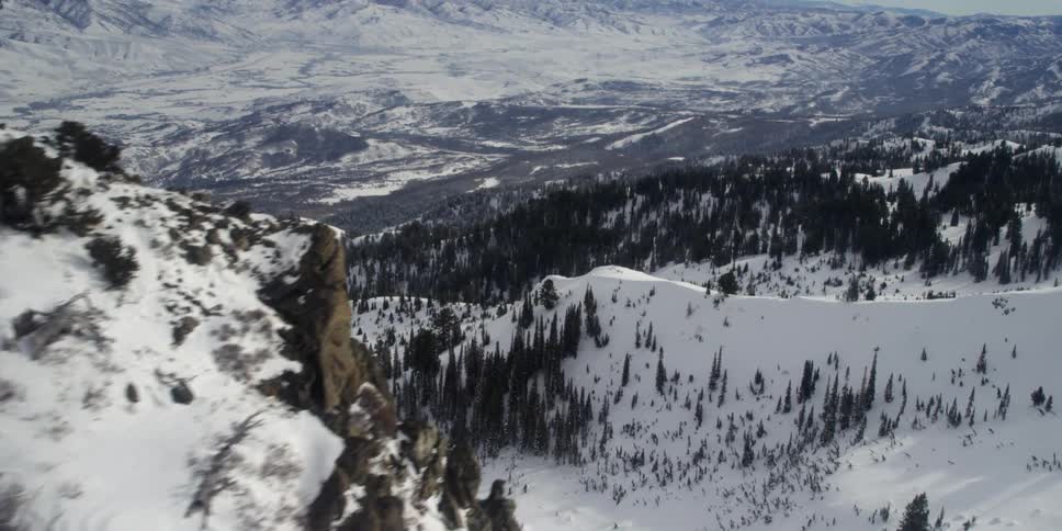 A snow covered mountain peak hides an enormous valley speckled in trees