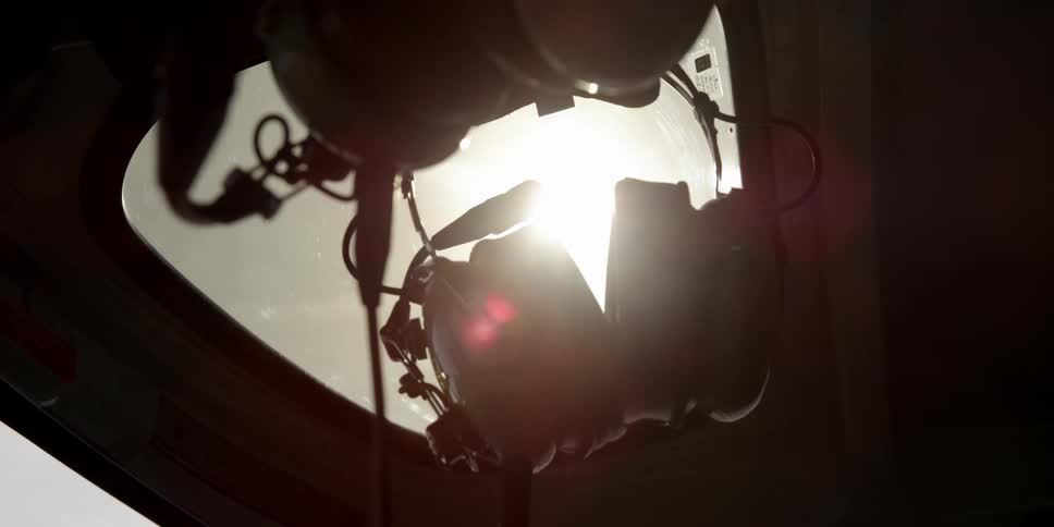 A radio headset hangs inside a helicopter near the window with the sun glaring