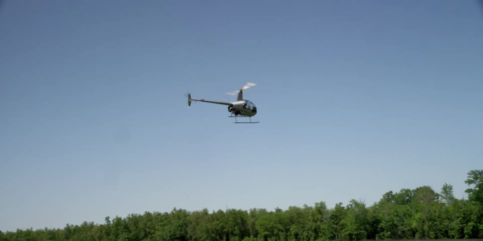 Helicopter with large blades going round very fast on top flies over trees and a river