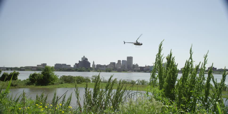 Helicopter flies over a river near the city buildings