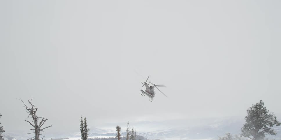 A helicopter flying low over a snowy countryside