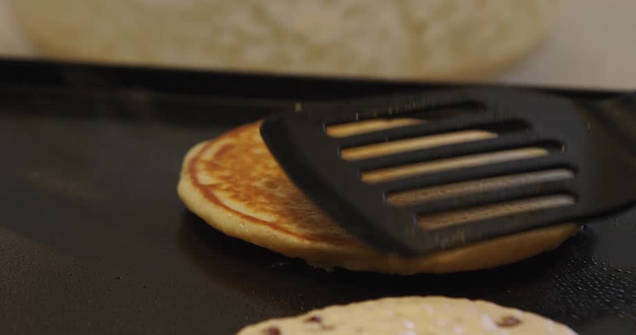 A spatula flips a pancake on a metal griddle