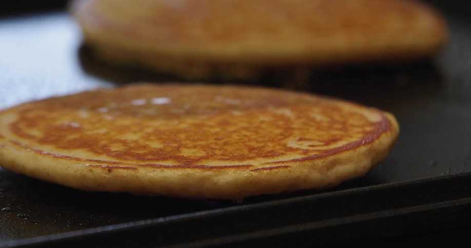 Spatula flips pancakes on oiled black girdle