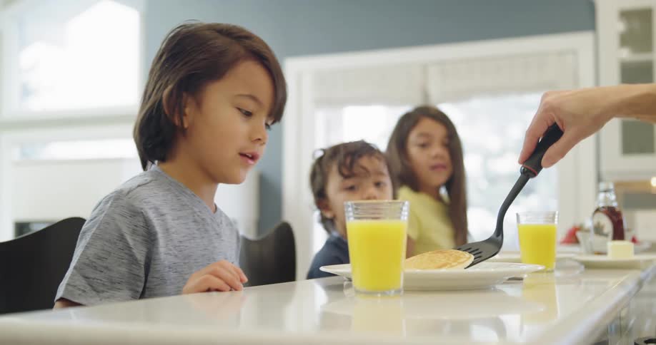 A woman serves a pancake to her son as his siblings look in