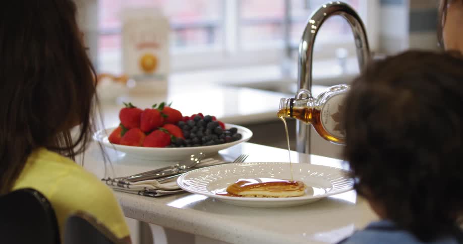 Maple syrup being poured on pancakes at breakfast