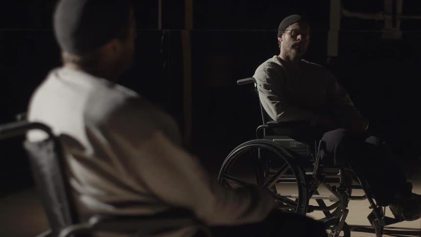 A man sits in a wheelchair while looking at his reflection in a mirror