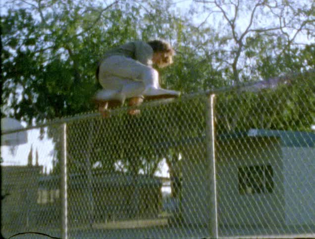 A white male teenager hops over a fence in a park