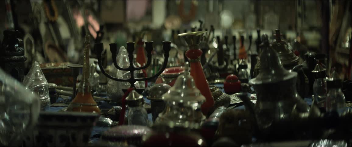 A large number of metal and glass objects sit on a table inside a store