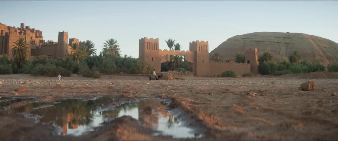 A person rides a horse past architecture as another person walks by