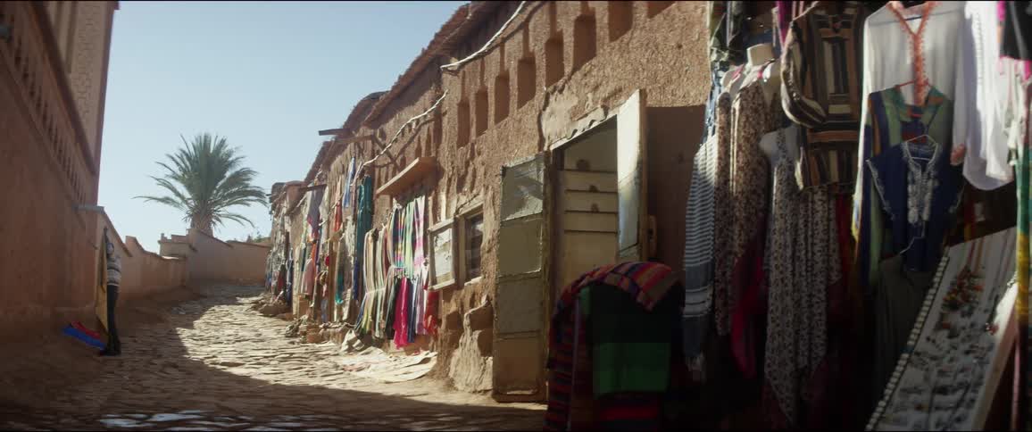 A man lies a blanket out across from an outdoor market in a village