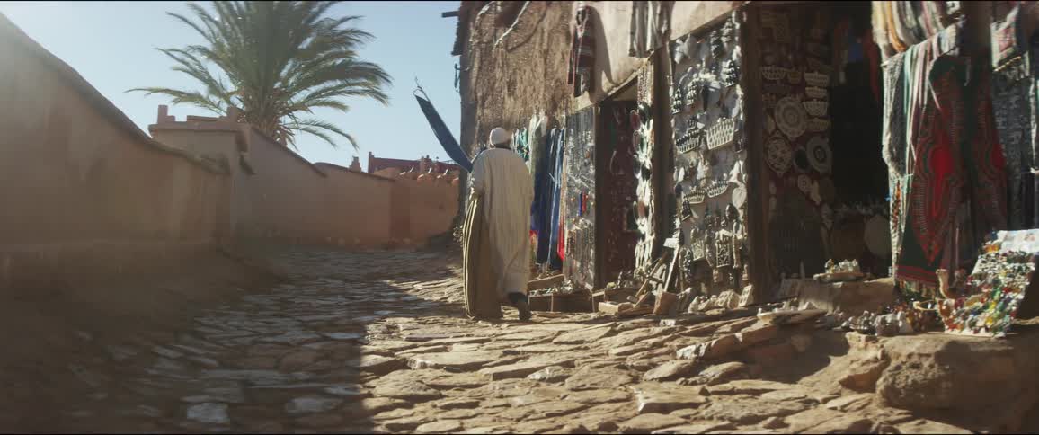A man carries a cloth bag as he walks past buildings on a rocky path