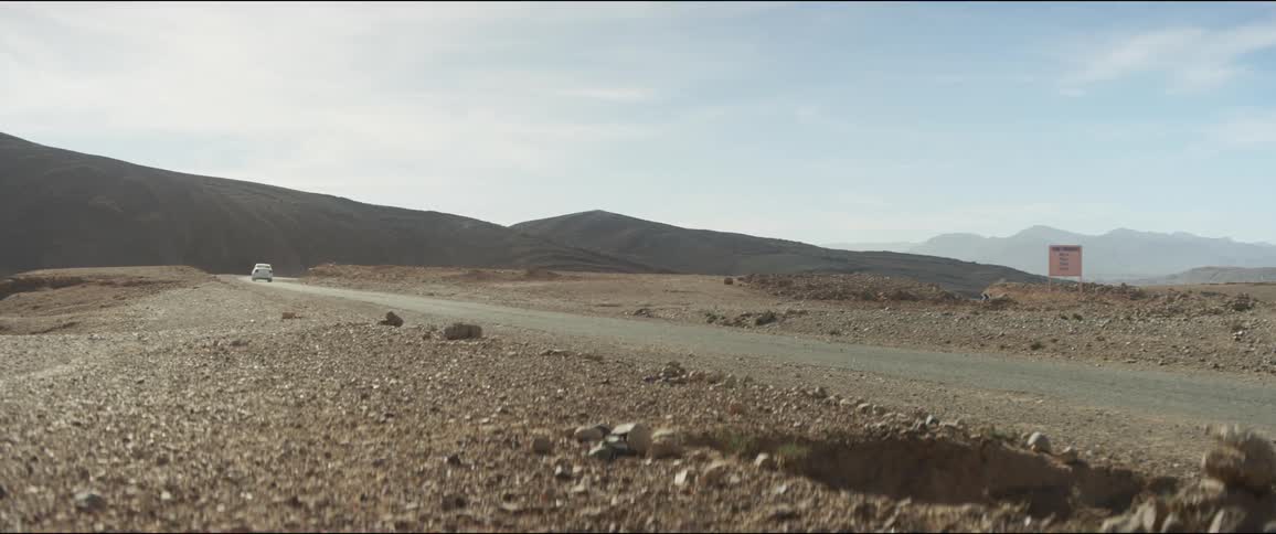 A car travels along a narrow asphalt mountain road during the day