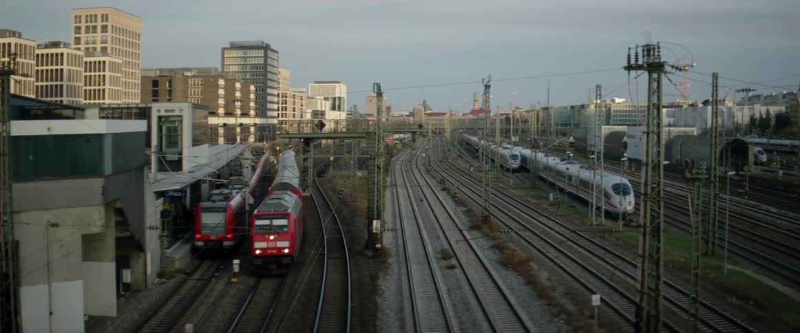 A red train lumbers down tracks running through a rail yard near the downtown area of a city