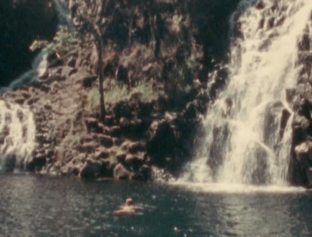 A person swimming in a creek next to two waterfalls