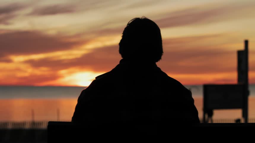 Man standing and watching the sun going down is silhouetted against sunset