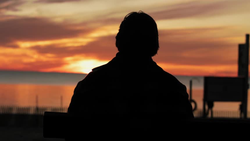 A man is standing outdoors watching the sunset