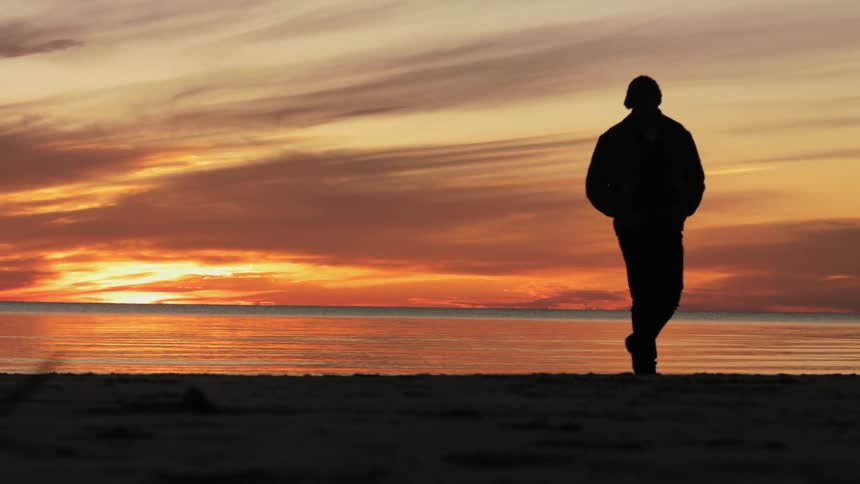 Man walking along the coast is silhouetted against the sunlight at sunset