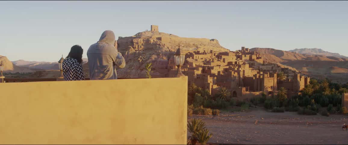 Two people standing on a rooftop overlooking a small village
