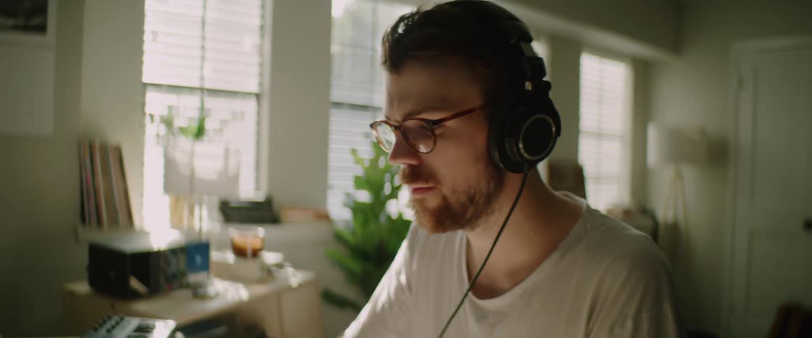 A man wearing headphones nods to the music as he sits in his home studio