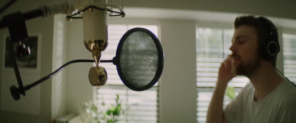 A man sings into a microphone in a home music studio