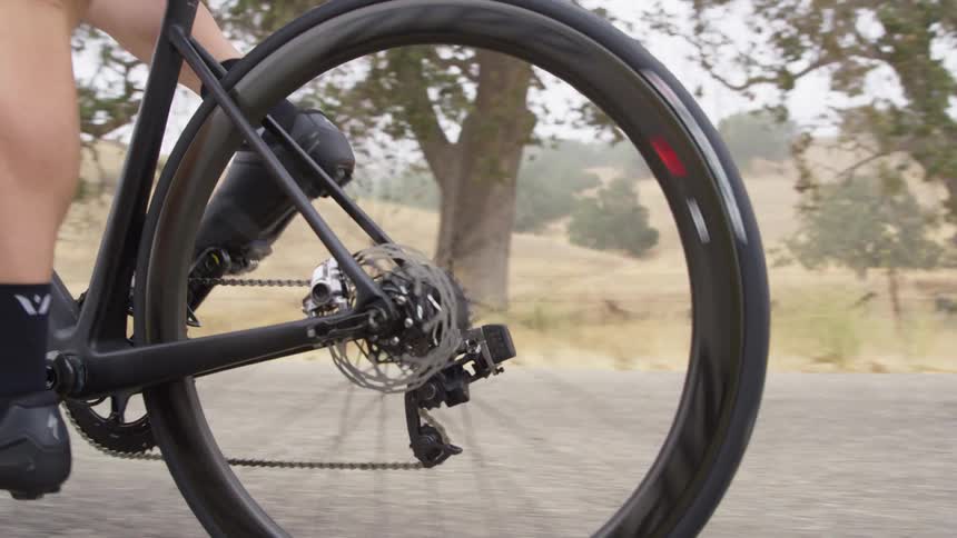 A cyclists legs pedal a bike on an empty rural road