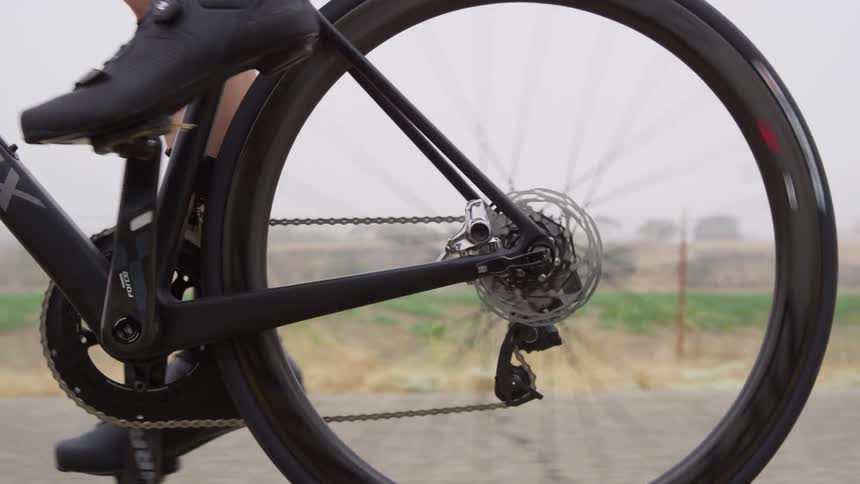 A mans feet pedaling a bike on a road with a grassy field and the sky in the background