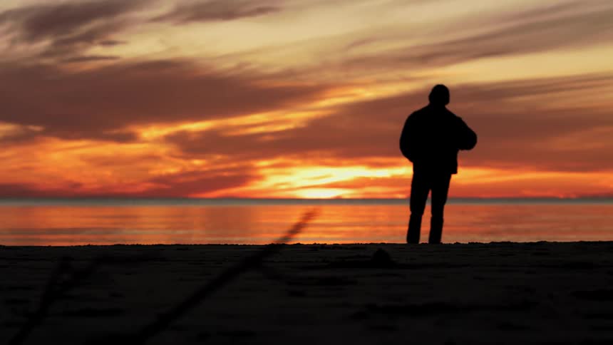 Man standing and watching the sun going down over the sea is silhouetted against sunset