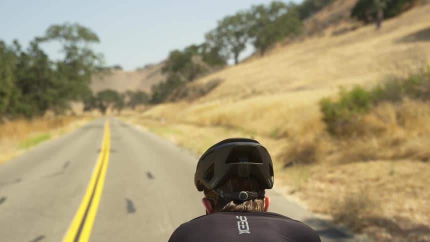 Male cyclist with black helmet and jersey rides a bicycle on a highway
