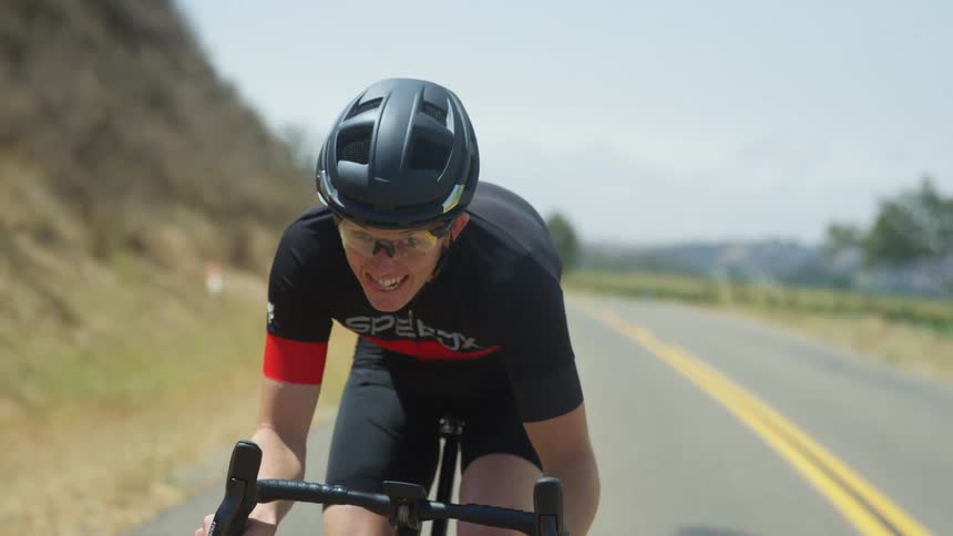 A male cyclist with mbt helmet and cycling jersey cycles uphill on highway next to a mountain