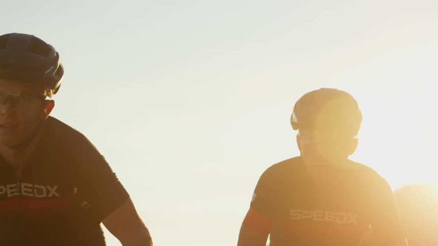 Cyclists with cycling helmet and cycling jersey rides bicycles on a road at sunset