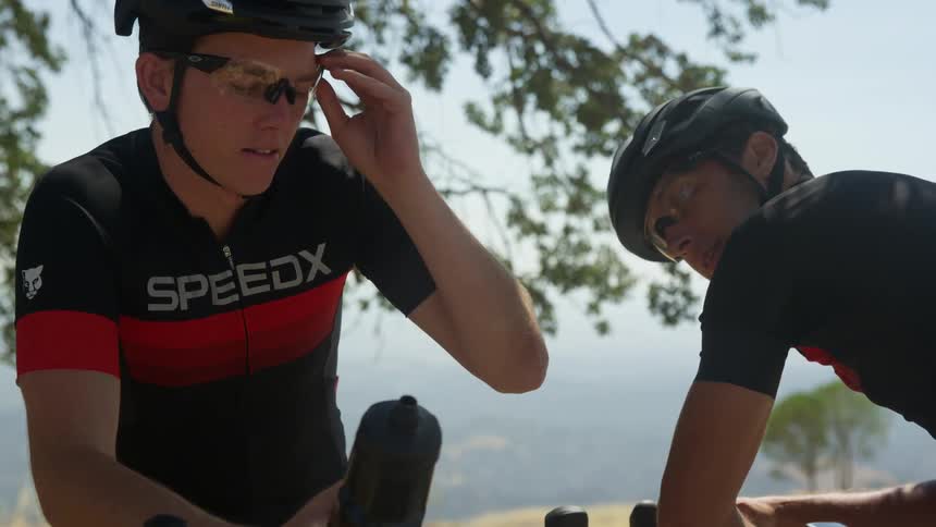 Two men on bikes wearing helmets and talking with trees and the sky in the background
