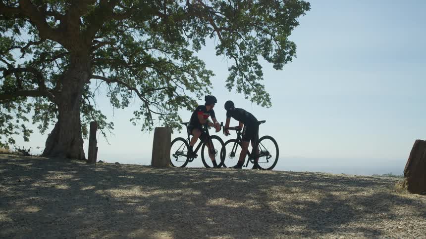 Two bicyclists rest and chat at a roadside rest area