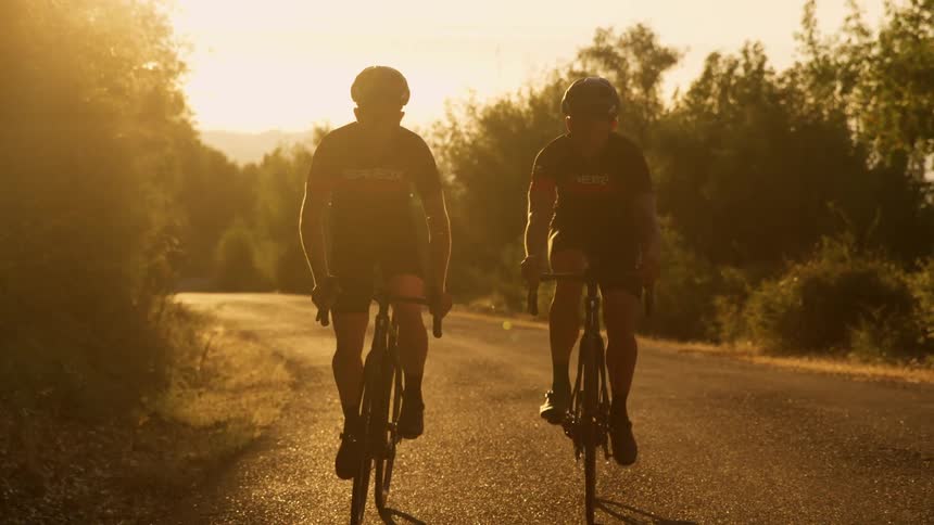 Silhouette ofcyclist riding up a mountain road against the sunlight