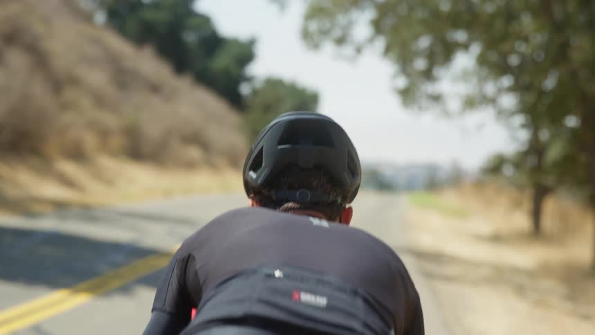 A determined male cyclist with black helmet and jersey rides a bicycle on a highway