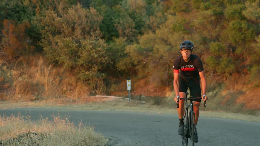 A man riding a bicycle down a narrow road through a hilly countryside