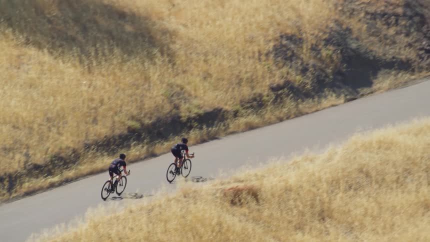 Bicyclists follow road between hills covered with yellow brown grass