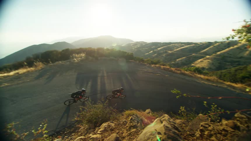 Two white males ride bicycles around a turn on a rural road