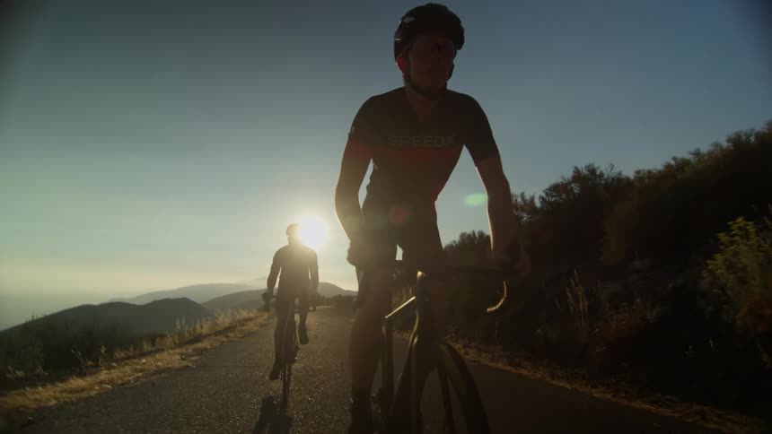 Cyclists with cycling helmet and cycling jersey ride bicycles on a mountain road at sunset